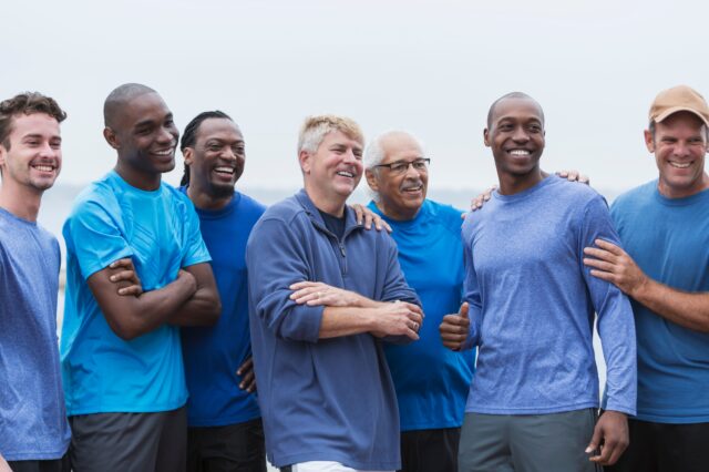 A group of men standing on a beach wearing blue shirts and smiling at the camera.