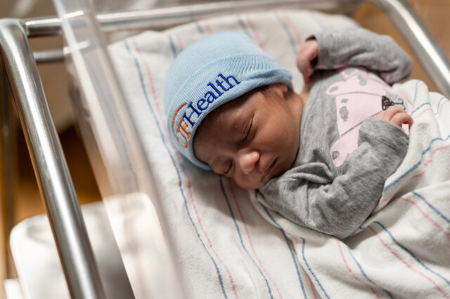 Newborn with a UF Health beanie on its head
