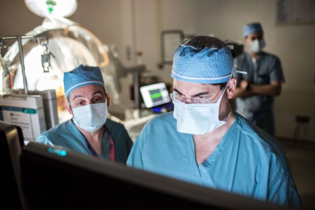 Dr. Kelly Foote & Dr. Michael Okun refer to a monitor while performing a deep brain stimulation procedur.