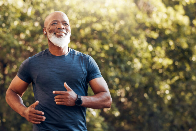 An older man with dark skin complexion jogging in a forest