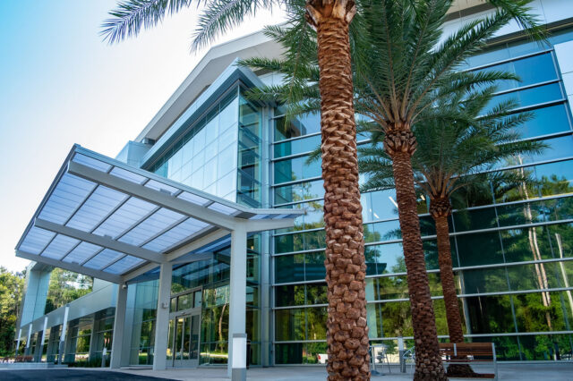 The exterior of Springhill Building 2. Blue-green glass and steel reflect palm trees and the forest that surrounds the building.