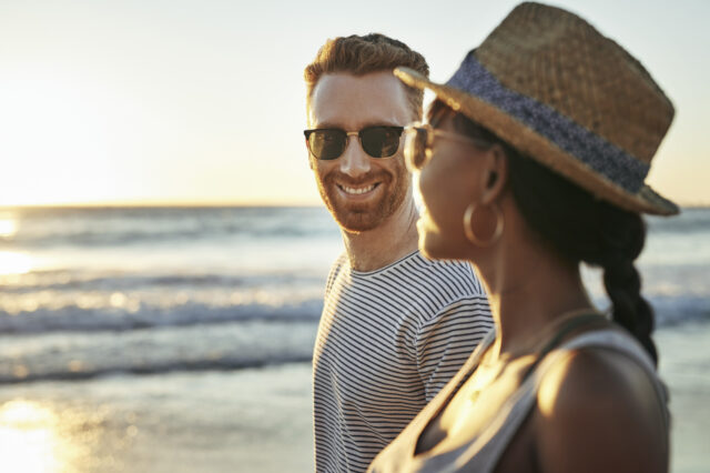 man and woman smiling and walking on beach