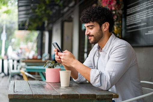 Person sitting at a cafe table looking at his phone