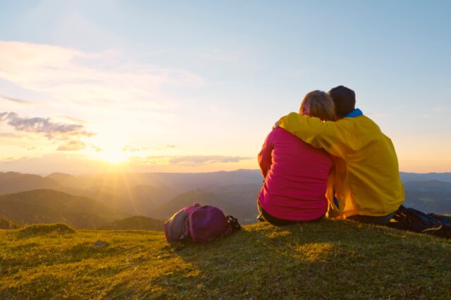 A couple stares at a sunset from on top of a mountain.