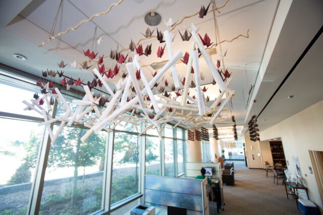 Hundreds of paper cranes hang from the roof of a large open space with desks and bookcases.