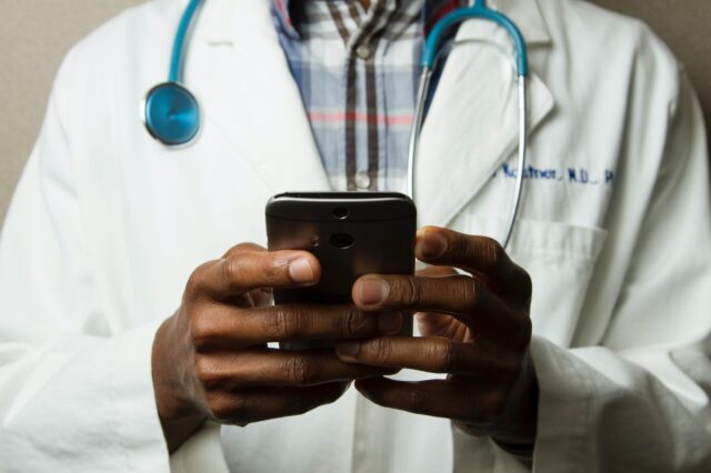 A doctor wearing a medical coat types on a cellphone