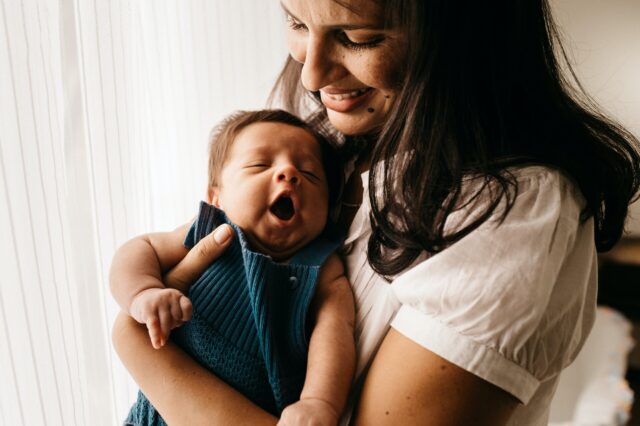 A woman holds a yawning newborn.