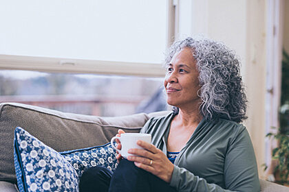 An older Hawaiian woman sitting on a couch holding a cup of coffee and looking into the distance