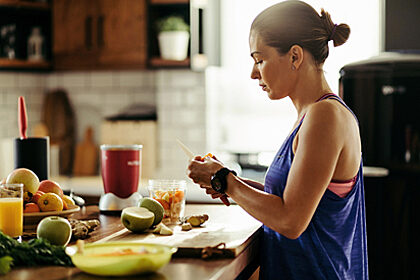 Woman in athletic clothing standing at a kitchen counter cutting fresh fruit for a smoothie
