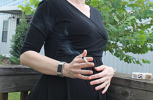 Pregnant woman holding belly and cigarette