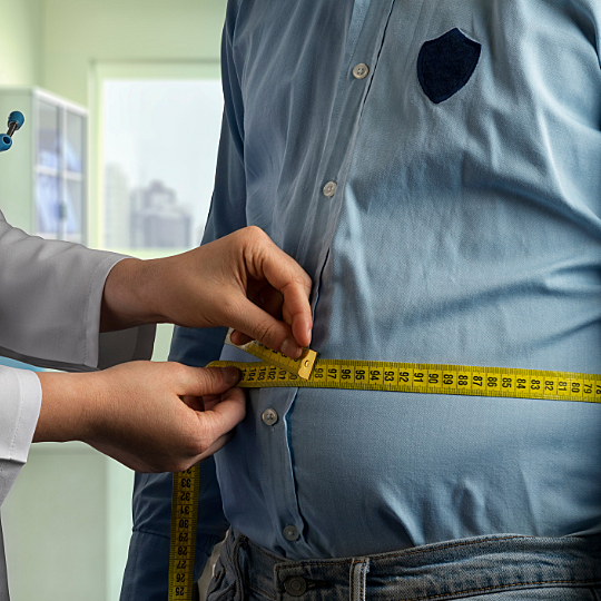 Stock photo: a physician encircles a man's midsection with a tape measure
