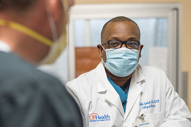 Dr. Adrian Tyndall, wearing mask, talks to another Uf Health caregiver
