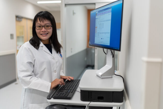 Doctor standing in front of computer screen smiling at camera