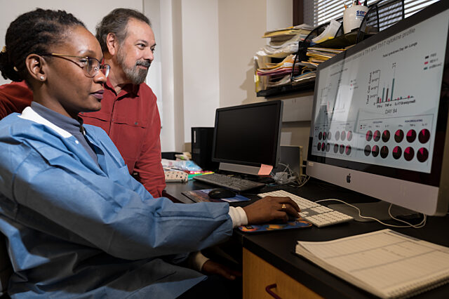 Two researchers sit at a computer looking at graphs and data.