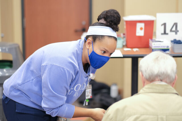 A health care professional helps administer a COVID-19 vaccine.