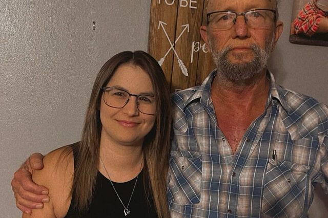 A brown-haired daughter stands next to her bald, bearded father.