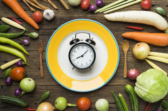 Stock image picturing an old-fashioned alarm clock centered on a plate and surrounded by vegetables