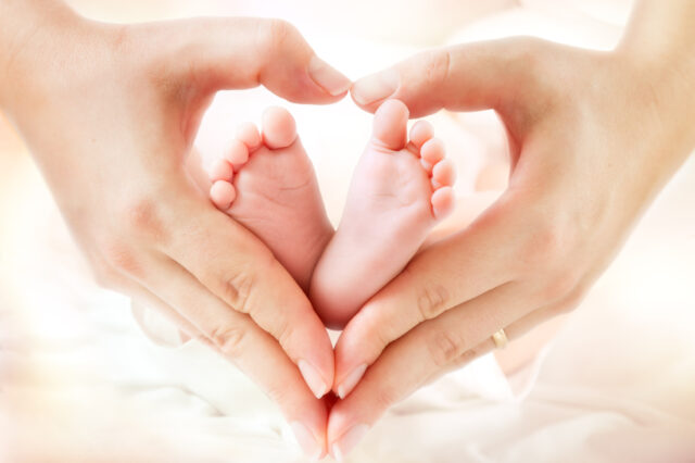 two hands making a heart around two baby feet
