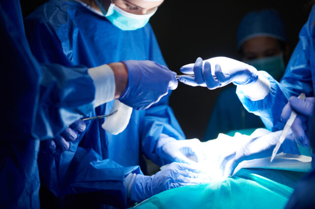 A surgeon passes scissors to another surgeon in the operating room