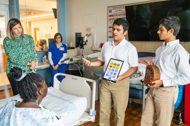 Aarin, seen with the tablet, and his brother Aarav demonstrate ICUSpeak to a patient during one of their visits to UF Health.