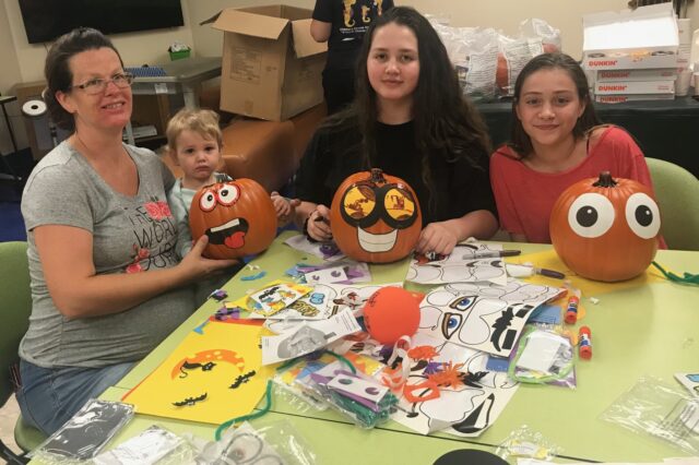 three children and an adult sitting at a table decorating pumpkins