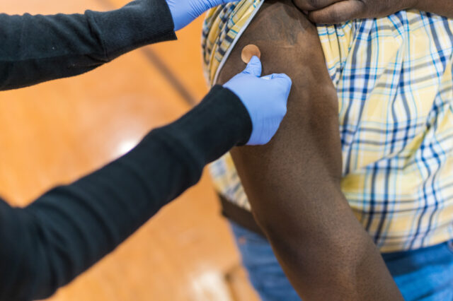 Savine Hernandez, Pharmacist Intern, places a bandaid on the arm of Leonard Johnson after he received his Covid-19 vaccine at Mt. Carmel Church in Gainesville, Fl.