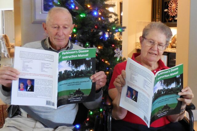Jane Masterson and Ed Smith sit in their living room in front of a Christmas tree. Each of them is reading a copy of their book, "Our Parkinson’s Disease Instruction Manual."