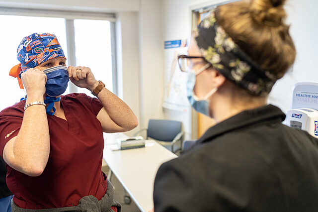 Two women health care providers talk while wearing masks and scrubs.