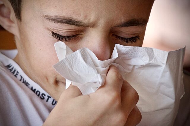 Boy sneezing into a tissue