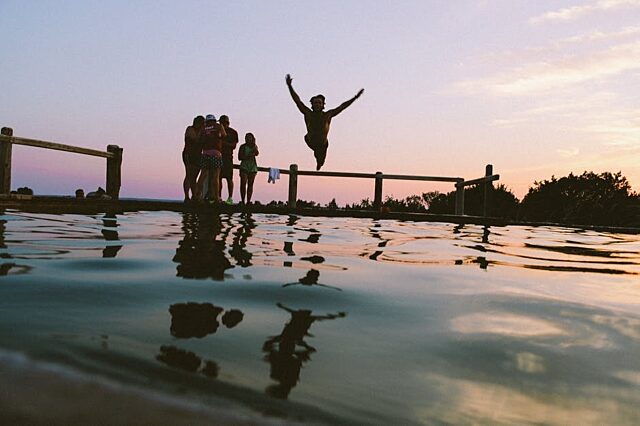 Beautiful sunset image featuring fun-loving, young adults at a lake with one young man leaping into the water with arms outstretched