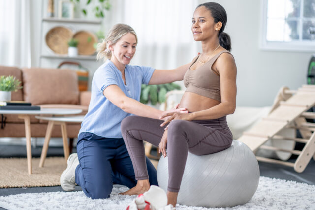 Pregnant patient on a workout ball with a therapist beside her