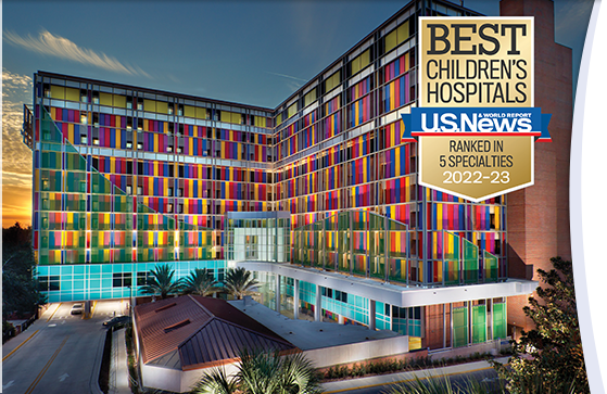 A sunset dramatically backlights the UF Health Shands Children's Hospital. Exterior lights highlight the red, blue, yellow, and purple panels that cover the face of the building in a patchwork pattern. The 2022-2023 U.S. News & World Report badge we earned for ranking in 5 specialties sits over the image. 