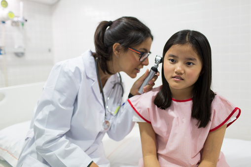 A female otolaryngologist peers into the ear of a young girl with an auriscope.