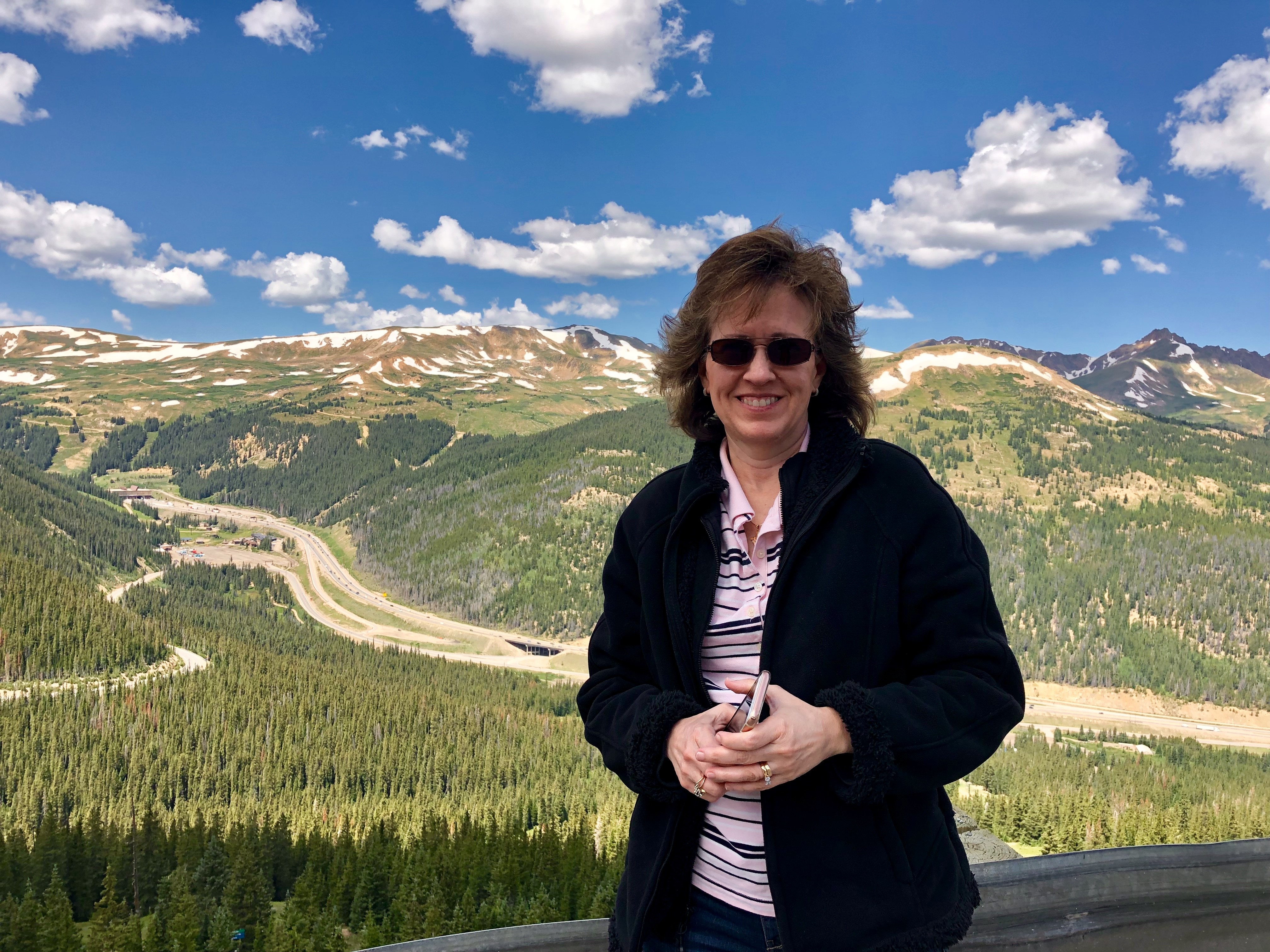 Kim Walliser is smiling at the camera with a mountain landscape in the background.