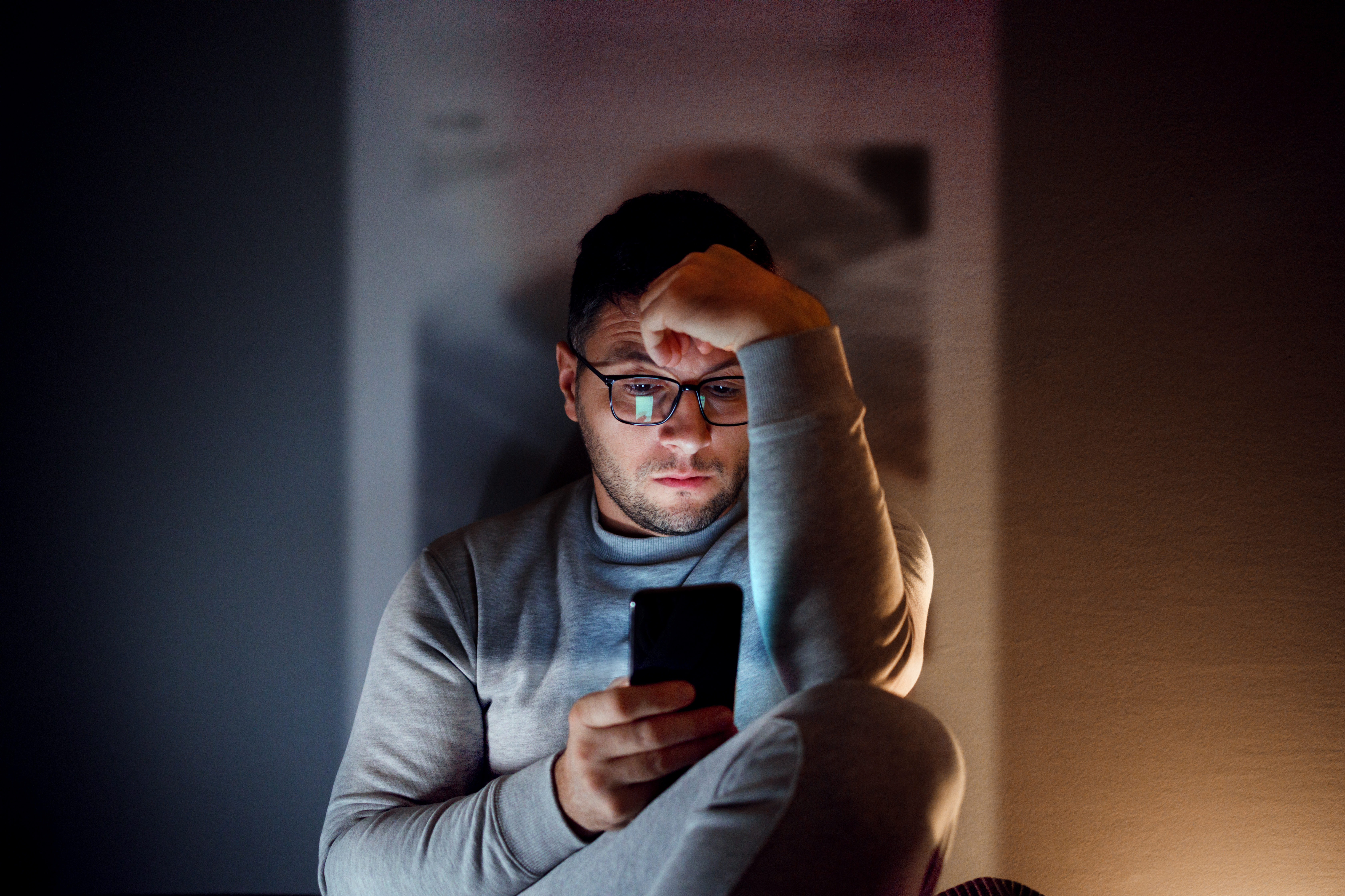 Man sitting in the dark and looking at a cellphone