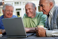 Three men sit gazing at a laptop computer.