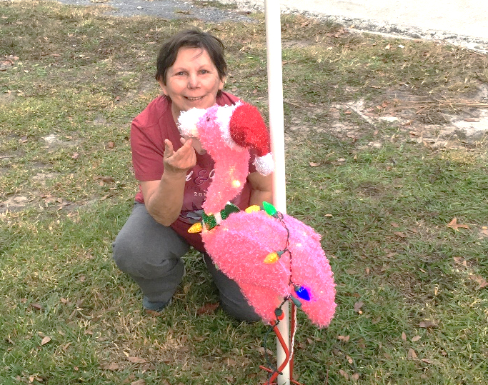 Judy crouching down on the ground posing with a flamingo Christmas decoration wearing a santa hat