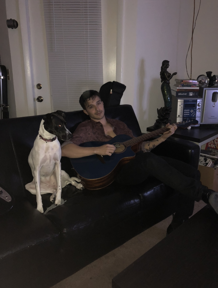 dylan lambert playing a guitar on a couch sitting next to a dog