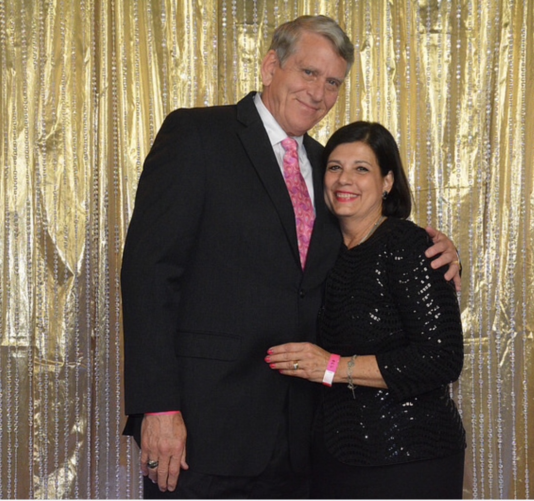 patient and his wife in formal wear posing in front of a gold backdrop