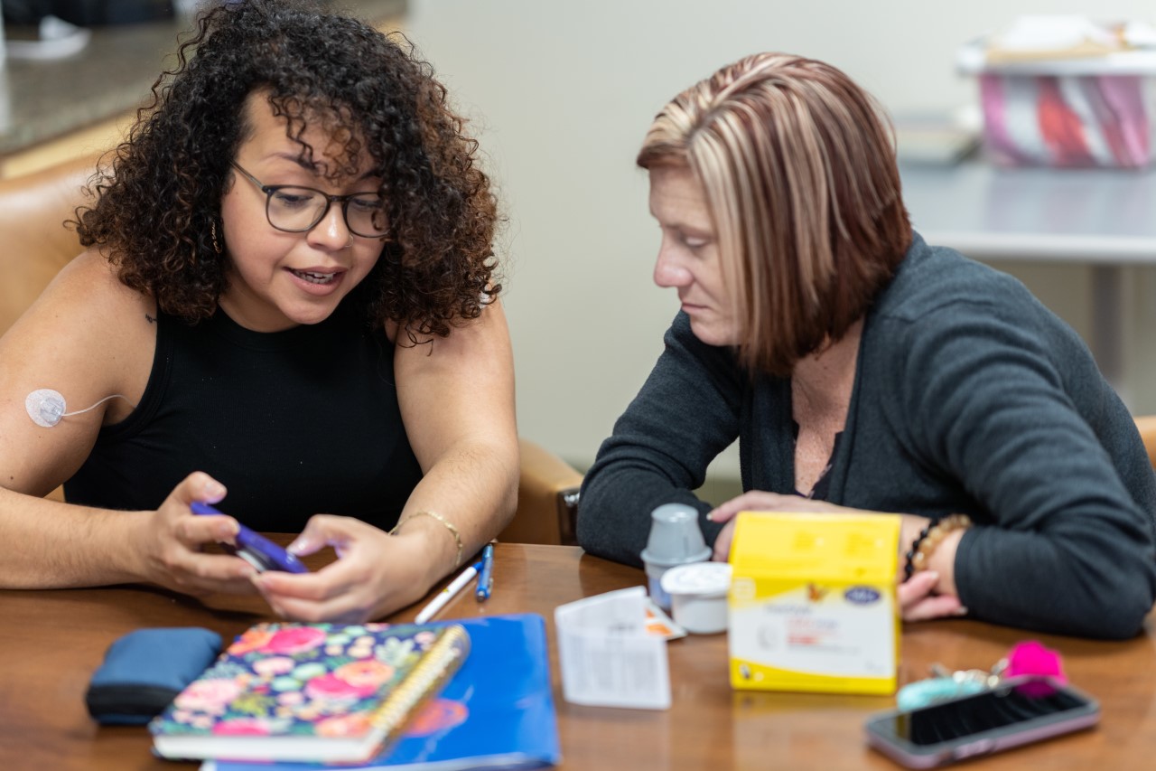 Roque shows Nichole Stephens how to track her blood glucose levels using an app during a meeting at UF Health Family Medicine – Old Town
