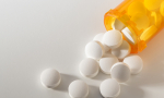 Stock image of white pills spilling from an amber pill bottle