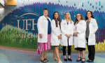 Five midwives, wearing white UF Health medical coats, stand in front of the tiled lobby wall in the UF Health Shands Children's Hospital.