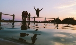 Beautiful sunset image featuring fun-loving, young adults at a lake with one young man leaping into the water with arms outstretched