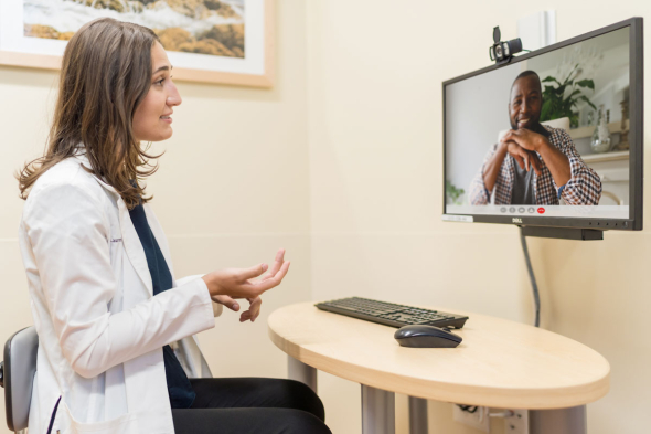 A health care professional talks to a patient using a video chat tool on a desktop computer.