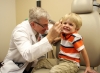 A photograph of a friendly, gray haired male doctor checking the right ear of a smiling, blond haired boy who is about five years old. Represents a new UF Health study questions the safety of antibiotic ear drops prescribed to children after ear tube surgery.